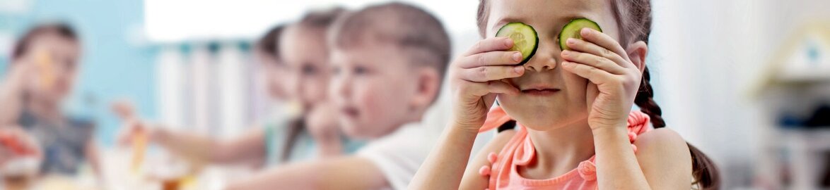 Kindergarten girl playfully holding cucumber in face